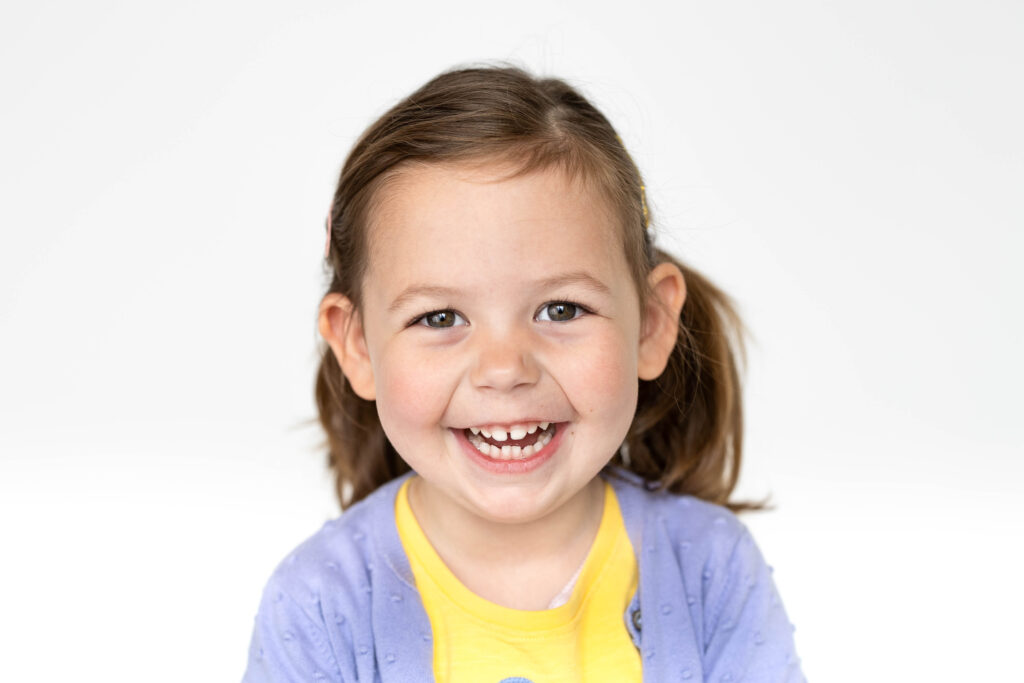 Smiling pre school aged child in a solid colored shirt on school picture day in Wayland, MA.